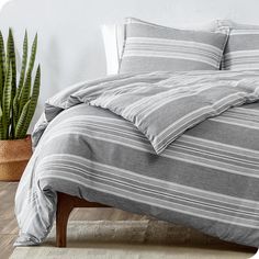 a bed with grey and white striped comforter next to a potted plant