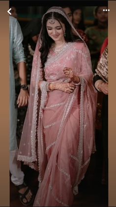 a woman in a pink sari walking down the street with her hands on her hips