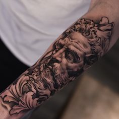 a man's arm with a black and white tattoo on it, depicting an ancient greek god