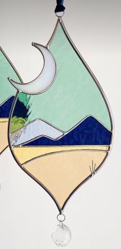 a stained glass sun catcher hanging on a wall with water and mountains in the background