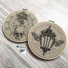 two embroidery hoops with designs on them sitting on top of a wooden table next to each other