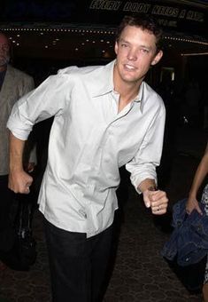 a man in white shirt and black pants holding his hand out to the side with other people