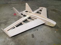 a wooden model airplane laying on the ground in an unfinished area with it's wings folded down