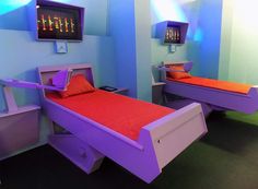 two beds in a room with blue walls and purple flooring, one has an orange pillow on it