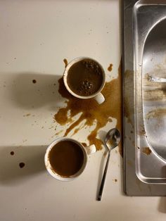 two cups of hot chocolate sit on a dirty counter next to a metal tray with spoons