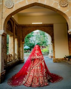 a woman in a red and gold bridal gown is standing under an arched archway