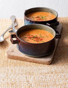 two pots of soup sitting on top of a wooden cutting board