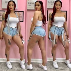 a woman with red hair wearing high waist denim shorts and white top, standing in front of pink wall