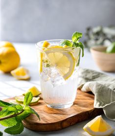 a wooden cutting board topped with a glass filled with ice and lemons next to sliced lemons