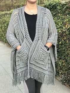 a woman standing on the sidewalk wearing a gray crocheted ponchy shawl