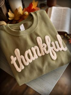 a green sweatshirt with the word grateful written on it next to an open book and autumn leaves