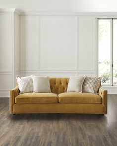 a yellow couch with pillows on it in front of a white wall and wooden floor