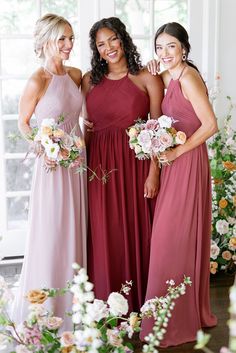 three women in long dresses standing next to each other and smiling at the camera with flowers