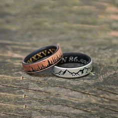 two rings with mountains and trees on them sitting on top of a piece of wood