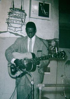 a man in a suit and tie playing an electric guitar while standing next to a microphone