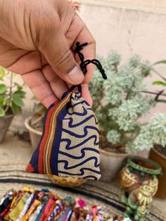 a hand is holding a small pouch filled with colorful bracelets next to potted plants