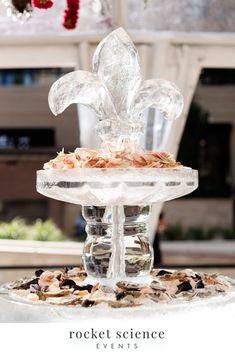 a glass water fountain with rocks and shells on it, in front of a window