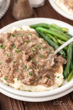 a plate with mashed potatoes, green beans and gravy on it next to a fork