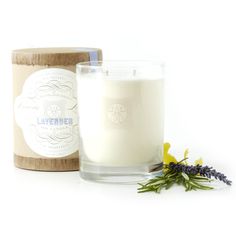 a glass candle next to a wooden container with flowers on the side and a label that says lavender