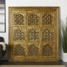 an ornately designed gold metal screen in a living room with a chair and potted plant