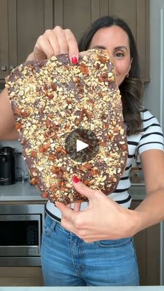 a woman holding up a piece of food with nuts on it in front of her face