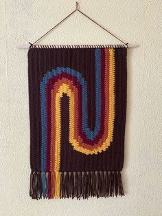 a crocheted wall hanging with multicolored stripes and fringes on a white wall