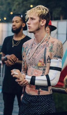 a man with tattoos on his arm holding a cell phone in front of other men