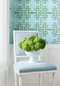 a white chair with a blue back and green flowers in the seat, against a wallpapered background