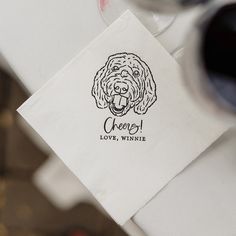 a paper napkin with a dog's face on it and the words cheers written in black ink