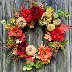 a wreath made out of fake flowers and pumpkins on a wooden fence with leaves