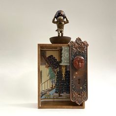 a miniature clock with a figurine on top of it's display case