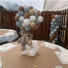 a teddy bear sitting on top of a table with balloons