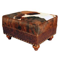 a brown and white cowhide ottoman with studded legs on an isolated white background