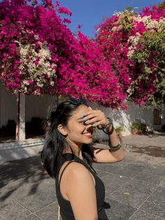 a woman standing in front of some pink flowers and holding her hand up to her face