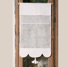 a window with a white curtain hanging from it's side and a potted plant on the other side