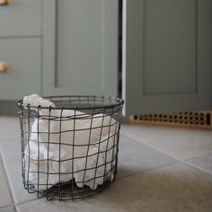 a wire basket filled with white towels on top of a kitchen floor next to cabinets