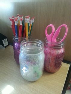 three jars filled with glitter and scissors on top of a table next to each other