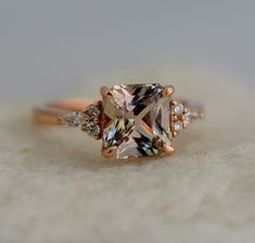 an engagement ring with three stones on the side and one stone in the middle, sitting on top of a white surface