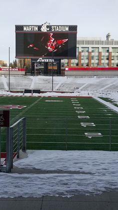 an empty football field with snow on the ground and a large scoreboard in the background