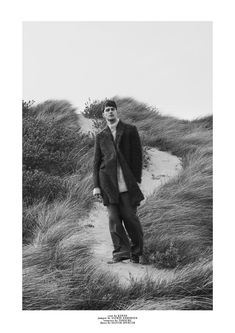 a black and white photo of a man standing in the sand dunes with his hands in his pockets