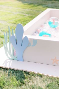 an empty box filled with plastic toys on top of green grass next to a fake cactus