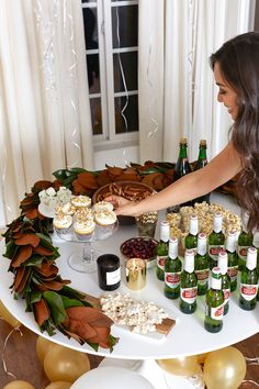 a woman is reaching for some food on a table with bottles of beer and desserts