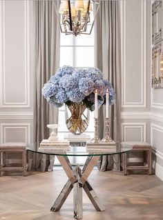 a glass table with flowers and candles on it in front of a chandelier