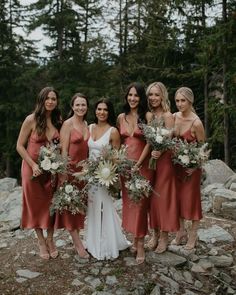 a group of women standing next to each other on top of a rocky hillside holding bouquets