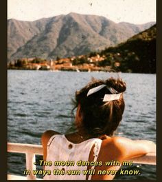 a woman sitting on top of a boat looking out at the water with mountains in the background