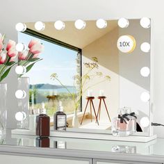 a large mirror with lights on top of it next to a vase filled with flowers