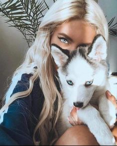 a woman holding a white and black husky dog with blue eyes in front of her face