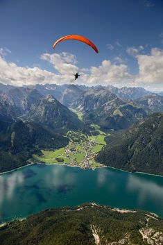 a paraglider flying over a lake surrounded by mountains in the distance with a bird's eye view