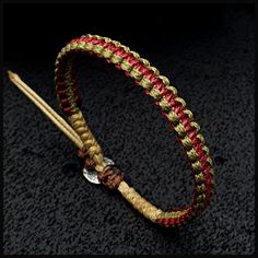 a red and gold braided bracelet with a metal hook on the end, sitting on a black surface