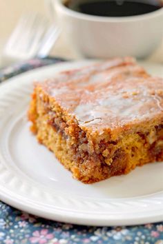 a piece of cake on a white plate with a cup of coffee in the background